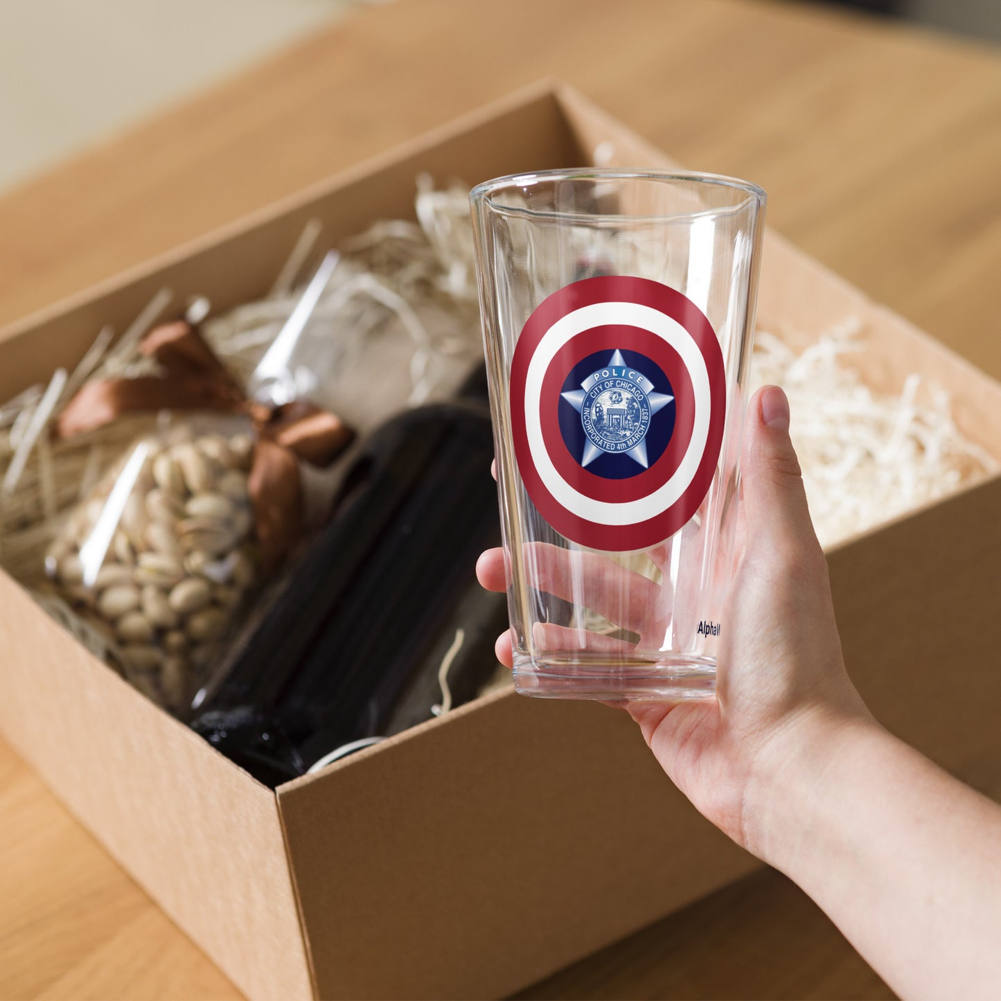 Hand holding a clear glass with a red, white, and blue emblem above an open box containing snacks.